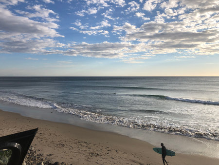 Surfer Enjoying the Waves Under a Vibrant Sky at the Beach During Golden Hourの写真素材
