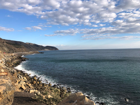 Coastal View at Sunset With Gentle Waves Lapping Against Rocky Shore in a Serene Landscapeの写真素材
