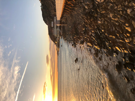 Sunset Over Rocky Shoreline With Vibrant Colors Illuminating the Ocean and Pier During an Evening Strollの写真素材