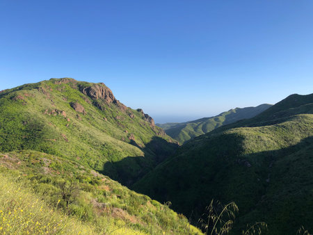 Scenic Mountain View Under a Clear Blue Sky in the Morning Light Showcasing Lush Green Hillsの写真素材