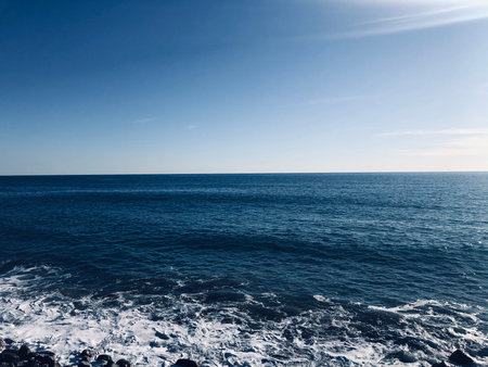 Calm Waves Gently Lap Against Rocky Shore Under a Clear Morning Sky at the Oceanの写真素材