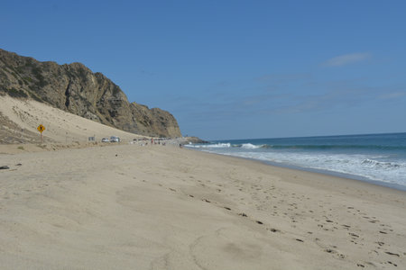 Sunny Beach Scene With Gentle Waves and Sandy Shores Near Rocky Cliffs on a Clear Dayの写真素材