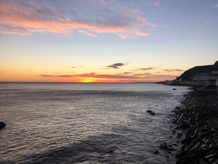 Beautiful Sunset Over the Tranquil Ocean Reflecting Vibrant Colors Near the Rocky Shore in a Peaceful Coastal Townの写真素材