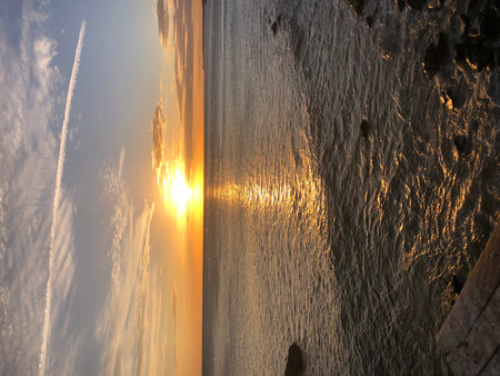 Golden Sunset Casts a Warm Glow Over the Tranquil Ocean Waves and Rocky Shoreline at Dusk Near the Coastの写真素材