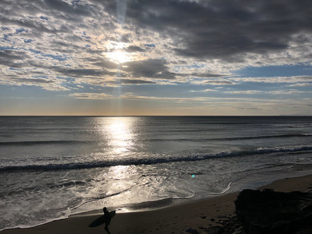 Sunset Beach Scene With a Lone Surfer Preparing to Catch Waves Along a Serene Coastlineの写真素材