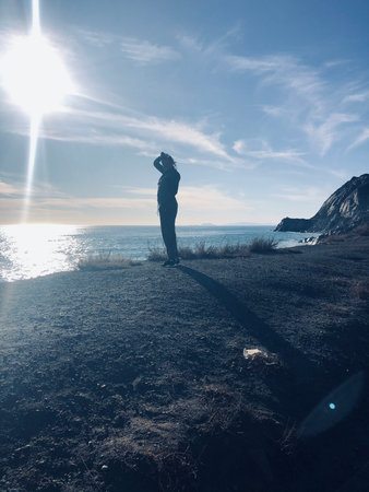 Exploring the Coastal Landscape at Sunset, a Figure Stands Quietly by the Shoreの写真素材