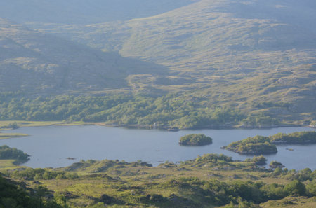 Expansive View of Lush Green Hills Surrounding a Serene Lake in a Tranquil Valley During a Sunny Afternoonの写真素材