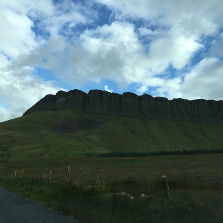 Majestic Green Cliffs Rise Against a Cloudy Sky During a Serene Afternoon Drive in the Countrysideの写真素材