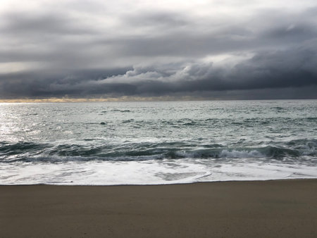 Stormy Waves Crash on a Tranquil Beach Under a Moody Sky at Sunsetの写真素材