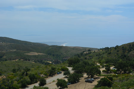 Scenic Mountain Landscape Reveals Winding Roads and Distant Ocean View Beneath a Soft Blue Skyの写真素材