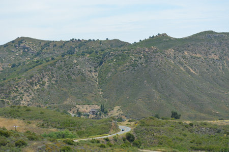 Winding Road Meanders Through Rolling Hills Under a Bright Blue Sky in a Tranquil Natural Landscapeの写真素材