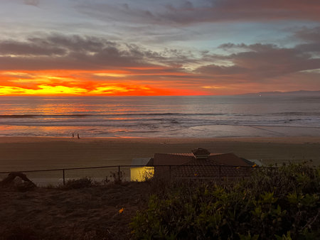 Sunset Glow Casts Vibrant Colors Over Serene Ocean Waves and Beachgoers Enjoying the Viewの写真素材