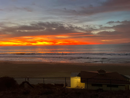 Vibrant Sunset Casts Colorful Reflections on the Ocean Waves Near a Peaceful Beachside Homeの写真素材