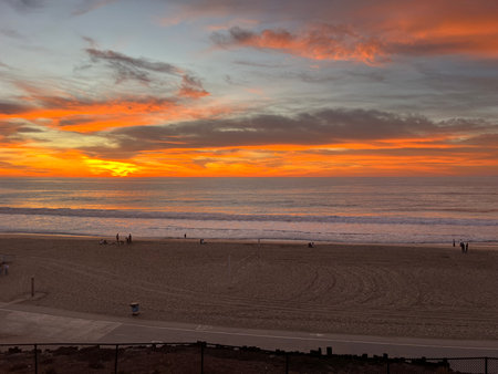Vibrant Sunset Paints the Sky Over the Tranquil Beach, Highlighting Playful Silhouettes of People Along the Shoreの写真素材