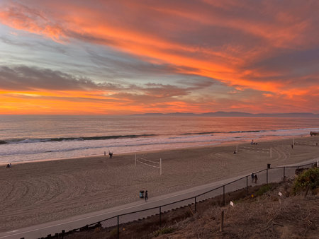 Sunset Over the Ocean Beach With Silhouettes of People Enjoying the Vibrant Colors in the Skyの写真素材