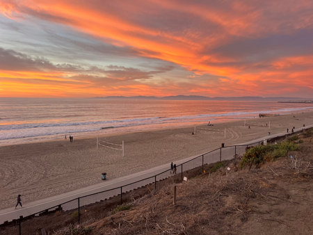 Beautiful Sunset Over the Beach With Volleyball Courts, People Walking, and Vibrant Colors in the Skyの写真素材