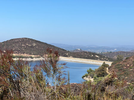 Scenic View of a Serene Lake Surrounded by Gentle Hills on a Bright Sunny Dayの写真素材
