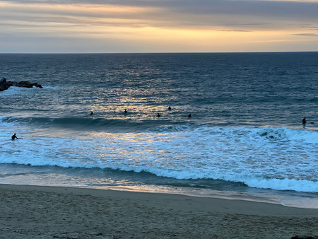 Surfers Enjoy the Calming Waves at Sunset by the Beach With Golden Clouds Aboveの写真素材