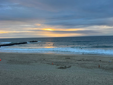 Beautiful Sunset Over the Ocean as Surfers Ride Waves on a Tranquil Beach in the Late Afternoonの写真素材