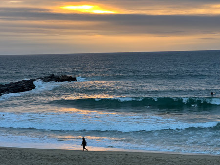 Sunset Glow Over a Serene Beach With a Lone Figure Walking Along the Shoreの写真素材