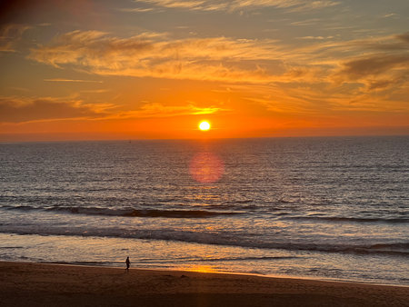 Sunset Over the Ocean Casting Warm Hues as a Solitary Figure Walks Along the Shore at the Beach in the Early Evening Glowの写真素材