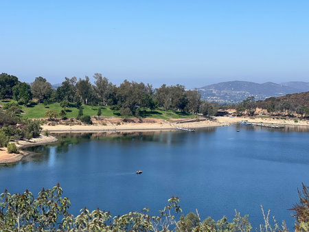 Scenic View of a Tranquil Lake Surrounded by Lush Greenery and Mountains on a Clear Sunny Dayの写真素材