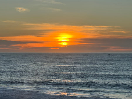 Warm Sunset Casts a Golden Glow Over Calm Ocean Waters at the Beach During a Peaceful Eveningの写真素材