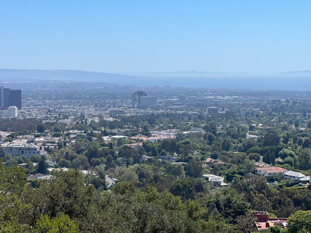 Scenic View of a Vibrant City Skyline Surrounded by Lush Greenery Under a Clear Blue Skyの写真素材