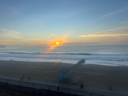 Sunset Over Tranquil Beach Waves With Surfers Enjoying the Evening and Sandy Footprints Leading to the Waterの写真素材