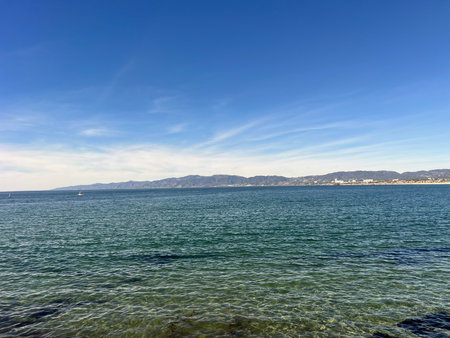 Scenic View of Calm Ocean Waters Reflecting the Clear Blue Sky Near Coastal Mountains on a Sunny Dayの写真素材