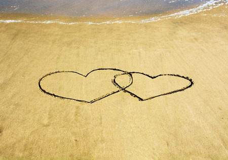 Two hearts drawn on the beach, waves in the distanceの写真素材