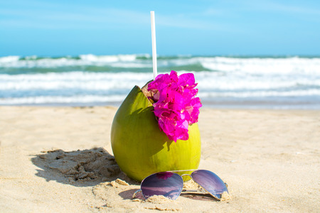 Green coconut with beautiful flower and sunglasses on the beachの写真素材