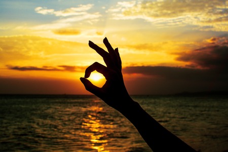 Ok hand sign silhouette at sunset. On bright sun background.の写真素材