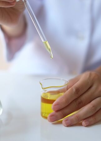scientist hand pour,drop oil or serum in the laboratory with leaves,equipment,glassware,cosmetic bottle.health and beauty natural organic product concept.herbal medicine. making cosmetic on table.の写真素材