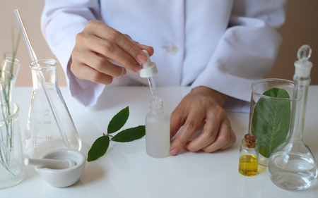 scientist hand pour,drop oil or serum in the laboratory with leaves,equipment,glassware,cosmetic bottle.health and beauty natural organic product concept.herbal medicine. making cosmetic on table.の写真素材