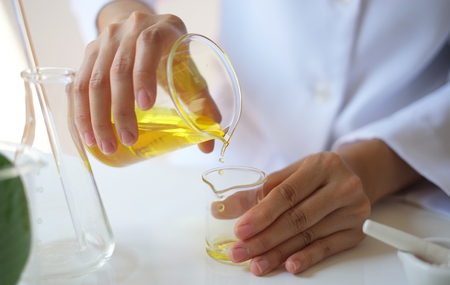 scientist hand pour,drop oil or serum in the laboratory with leaves,equipment,glassware,cosmetic bottle.health and beauty natural organic product concept.herbal medicine. making cosmetic on table.の写真素材