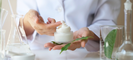 scientist hand giving  with leaves,equipment,glassware,cosmetic bottle.health and beauty natural organic product concept.herbal medicine. making cosmetic on table.の写真素材