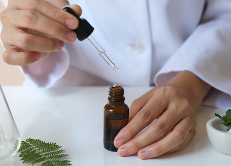 essential oil drop into the bottle. liquid  serum cosmetic and skincare . alternative medicine with leaf and laboratory . scientist hand.の写真素材