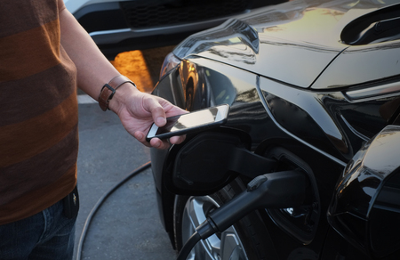 A man at the power supply for electric car charging station.  charging the battery of the vehicle and check the status and control with the mobile smart phone. の写真素材