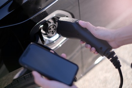 A man at the power supply for electric car charging station. charging the battery of the vehicle and check the status and control with the mobile smart phone.の写真素材