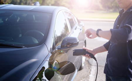 A man at the power supply for electric car charging station. charging the battery of the vehicle and check the status and control with the mobile smart phone.の写真素材