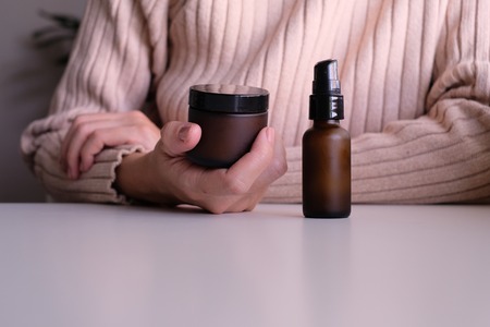 hand with cosmetic cream lotion .Beauty skincare background .Products with flower ,leaves . pink...