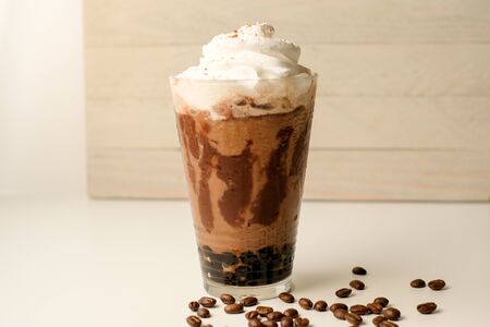 Ice coffee in the glass topped whipping cream with coffee beans. Cold summer drink on wooden...