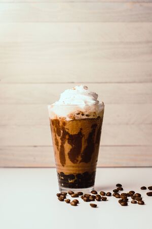 Ice coffee in the glass topped whipping cream with coffee beans. Cold summer drink on wooden background and copy space. Advertising for caramel mocha and chocolate beverage for the cafe.の写真素材