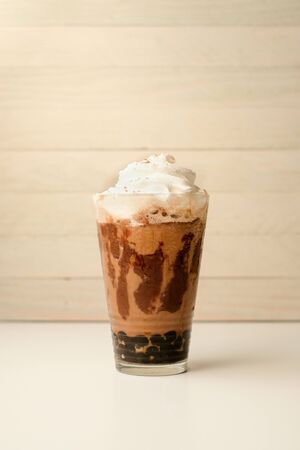 Ice coffee in the glass topped whipping cream with coffee beans. Cold summer drink on wooden background and copy space. Advertising for caramel mocha and chocolate beverage for the cafe.の写真素材