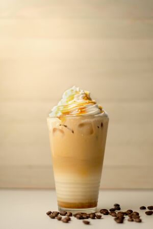 Ice coffee in the glass topped whipping cream with coffee beans. Cold summer drink on wooden background and copy space. Advertising for caramel mocha and chocolate beverage for the cafe.の写真素材