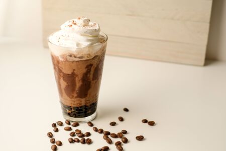Ice coffee in the glass topped whipping cream with coffee beans. Cold summer drink on wooden background and copy space. Advertising for caramel mocha and chocolate beverage for the cafe.の写真素材