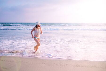 young woman on sunset beach and joyful running . happy summer vacation. positive lifestyle and relaxing travel. nature recreation.の写真素材