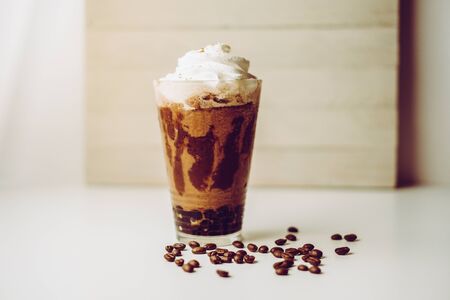 Ice coffee in the glass topped whipping cream with coffee beans. Cold summer drink on wooden background and copy space. Advertising for caramel mocha and chocolate beverage for the cafe.の写真素材