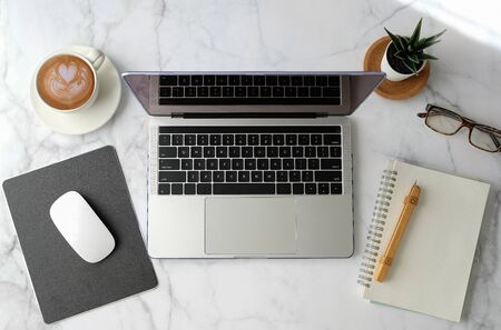 Flat lay workspace. Woman hand with coffee cup, smartphone, computer, notebook, planner and stationary with copy space on marble table background. Top view. modern style.の写真素材